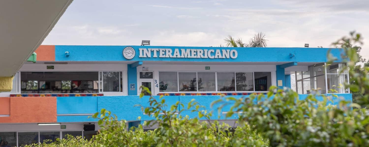 Fachada del Colegio Interamericano con distintiva estructura azul y naranja, amplios ventanales y zona arbolada.